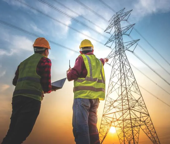 Engineers reviewing plans beside a transmission tower (contextual image)